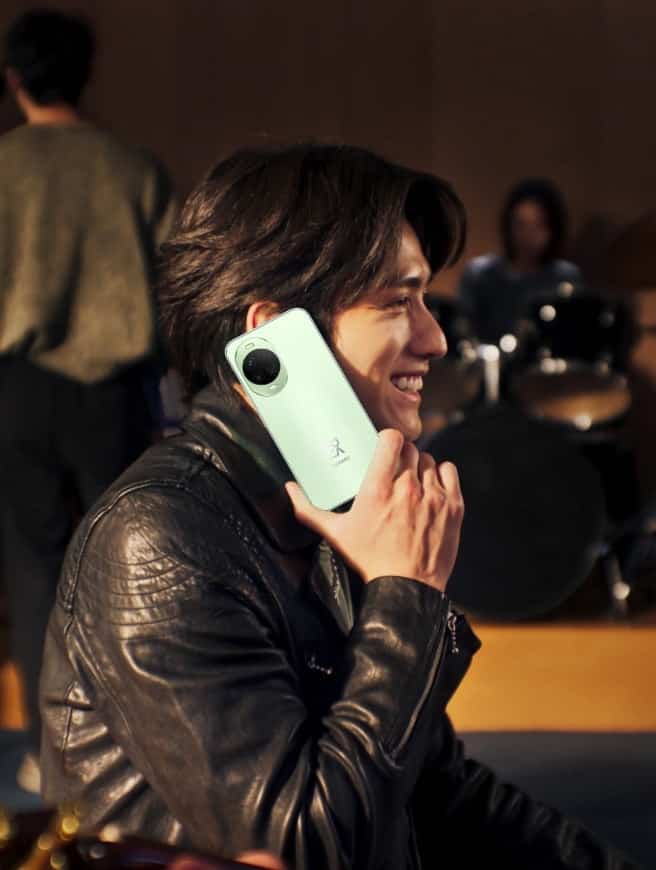 Мужчина держит зелёный Huawei Nova 15 у уха на концерте
